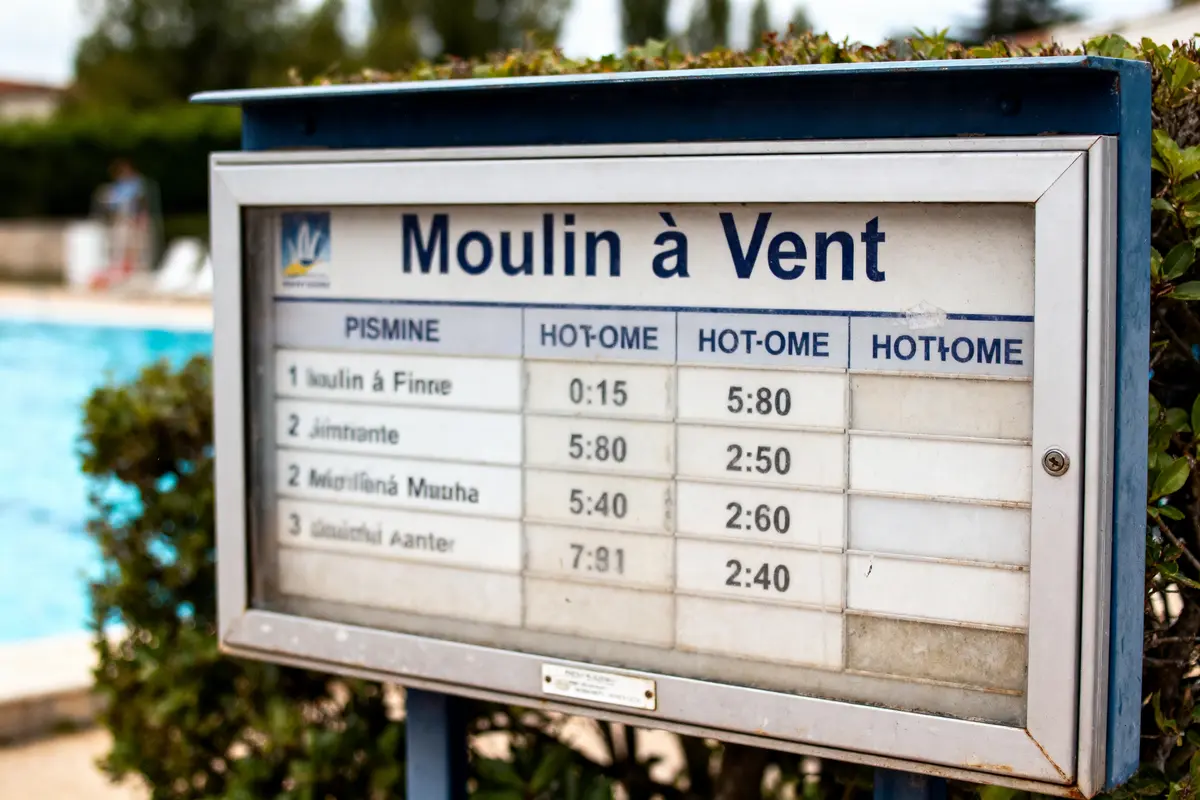 Panneau d'affichage extérieur près d'une piscine, indiquant horaires et tarifs à "Moulin à Vent".