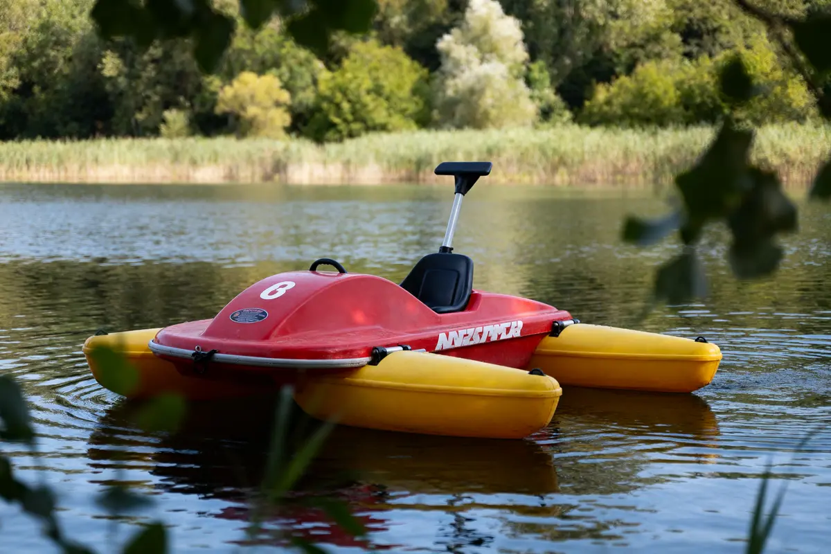 Pédalo rouge et jaune flottant sur un lac entouré de végétation verdoyante.