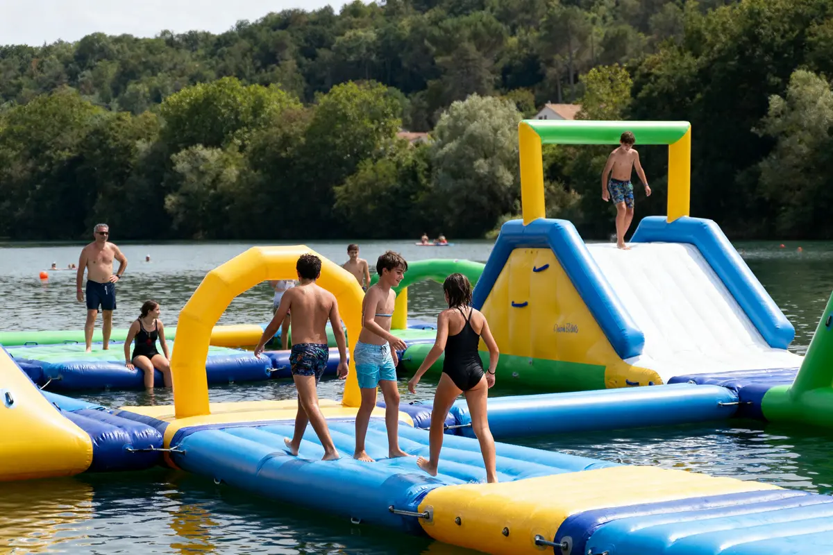 Personnes sur structure gonflable aquatique colorée, avec toboggan, entourées d'eau et de végétation. Activité estivale amusante.