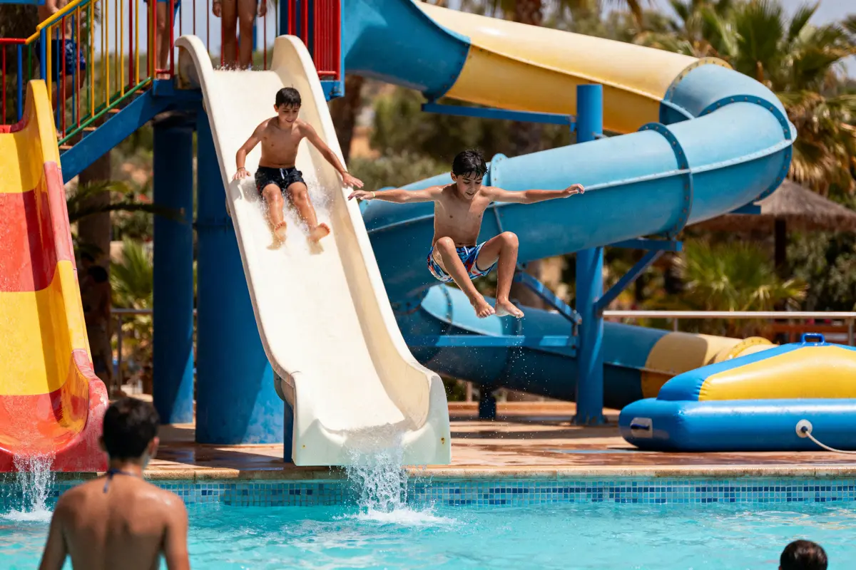 Deux enfants s'amusent sur un toboggan aquatique, éclaboussant dans la piscine en été.