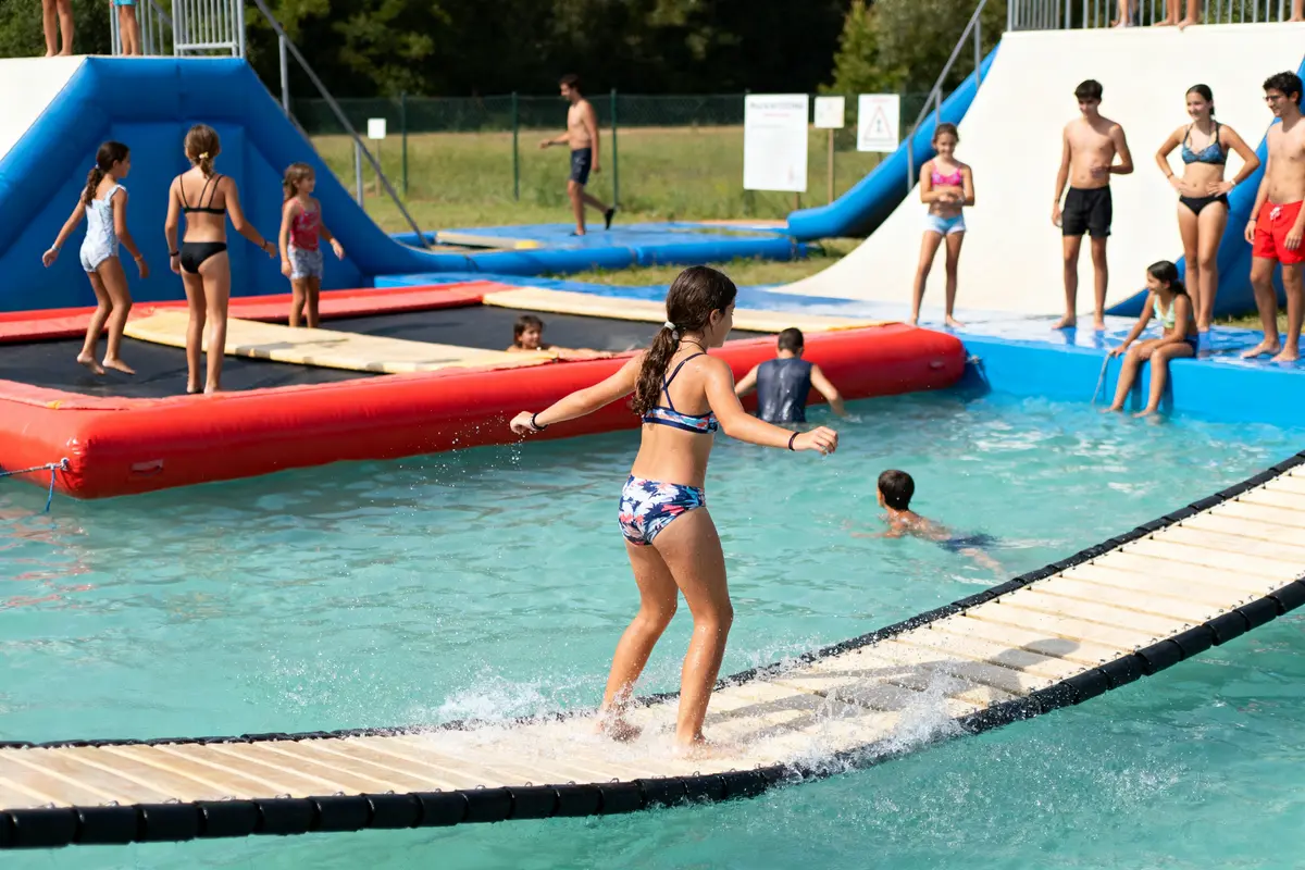 Enfants jouant et s'amusant dans une piscine avec des structures gonflables et toboggans aquatiques en extérieur.