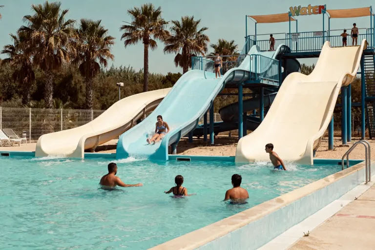 Personnes s'amusant sur les toboggans du parc aquatique Narbonne entouré de palmiers