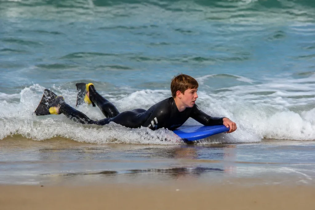 Jeune bodyboarder avec palmes prenant une petite vague près du bord
